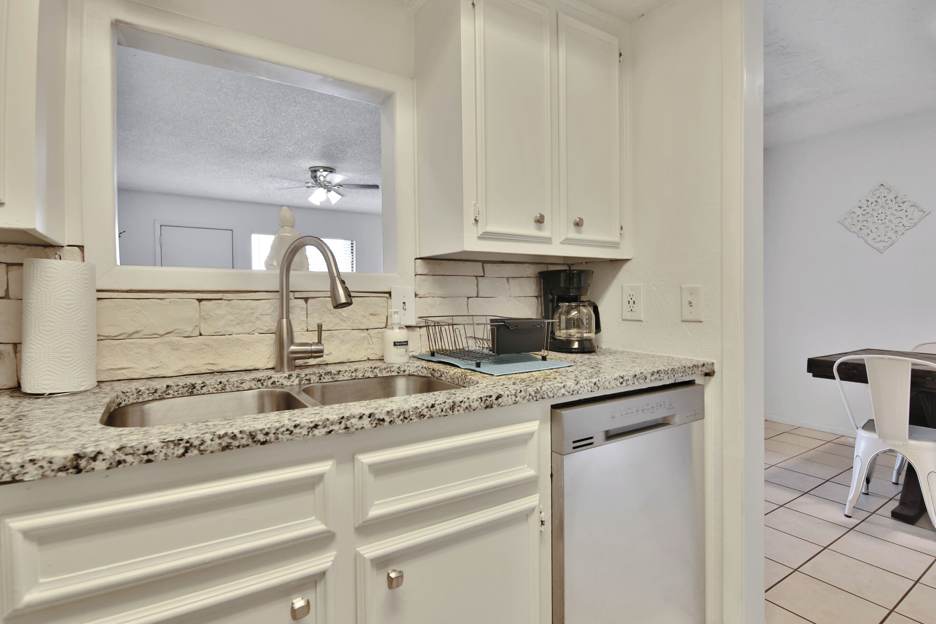 A kitchen with white cabinets, a double sink, a coffee maker, and a dishwasher.