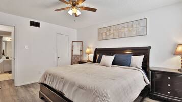 A bedroom with a bed, a ceiling fan, a nightstand, a lamp, a wall art piece, and a door.