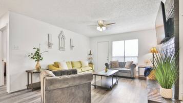 A spacious living room with a sofa, armchair, coffee table, and decorative plants.