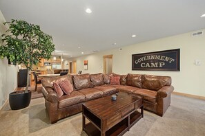 A living room with a brown leather sectional sofa, a coffee table, and a potted plant. - Laurel Hill Condo 303 at South Grand Lodge | Partial Mt. Hood View (Government Camp)