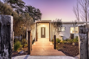 A wooden pathway leading to a house with a dark door, surrounded by trees and shrubs. - Manuka Bliss Heights - Close to Thermal Hoot Pool (Kaukapakapa)