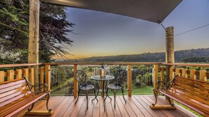 Una terraza de madera con una mesa y sillas, con vistas a un paisaje de árboles y colinas.