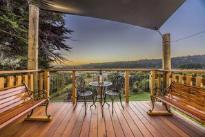 A wooden deck with a table and chairs, overlooking a landscape with trees and hills. - Manuka Bliss Heights - Close to Thermal Hoot Pool (Kaukapakapa)