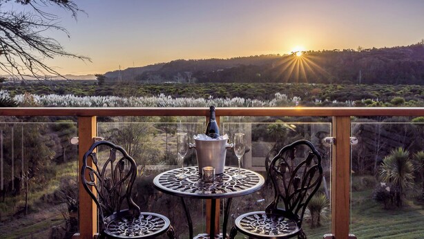 Un balcón con mesa y sillas, con vistas a un paisaje al atardecer.