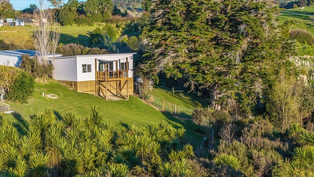A modern house with a deck, surrounded by lush greenery and trees.