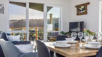A dining area with a wooden table set for four, surrounded by chairs, with a view of the outdoors through large sliding glass doors.