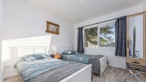 Un dormitorio con dos camas, una ventana con cortinas, una mesita de noche con lámpara y un espejo.