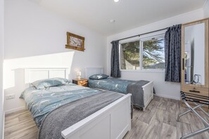 A bedroom with two beds, a window with curtains, a bedside table with a lamp, and a mirror. - Manuka Bliss Heights - Close to Thermal Hoot Pool (Kaukapakapa)