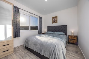 A bedroom with a bed, a nightstand, a wardrobe, and a window with curtains.