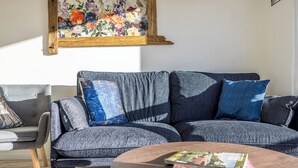 A modern living room with a grey sofa, a wooden coffee table, and a floral painting on the wall.