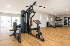 Ett gym med en mångsidig träningsstation, ett löpband och ett stort fönster som släpper in naturligt ljus.