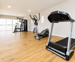 A gym with a treadmill, elliptical, and weight machines. - Cozy, fully equipped studio apartment with coworking space, gym, and great location. (Curitiba)