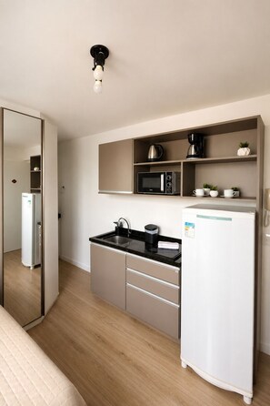 A compact kitchenette with a microwave, coffee maker, and a refrigerator. - Cozy, fully equipped studio apartment with coworking space, gym, and great location. (Curitiba)