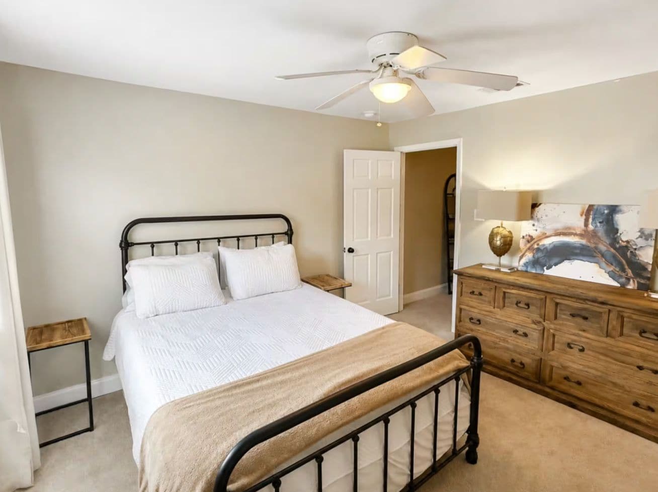 A bedroom with a bed, a dresser, a nightstand, a ceiling fan, and a door leading to another room.