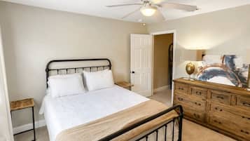 A bedroom with a bed, a dresser, a nightstand, a ceiling fan, and a door leading to another room.