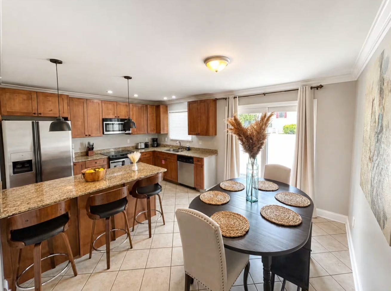 A modern kitchen with granite countertops, stainless steel appliances, and a dining area with a round table and bar stools.