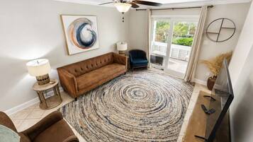 A living room with a brown sofa, a round rug, a ceiling fan, and a TV stand.