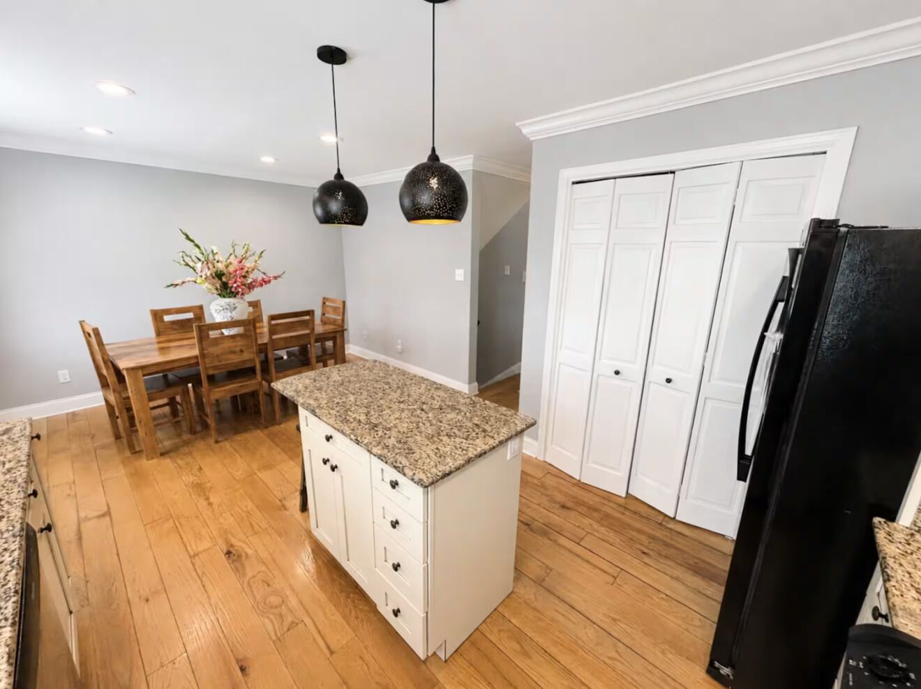 Une cuisine dotée d’un îlot central, d’une table à manger en bois, de chaises, de luminaires suspendus et d’un réfrigérateur.