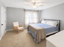 A bedroom with a bed, a chair, a nightstand, and a ceiling fan.