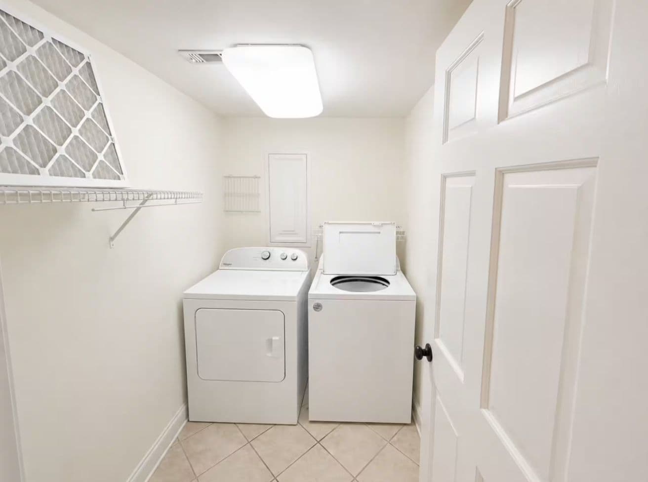 A laundry room with a washing machine and dryer, a window with a metal screen, and a door.