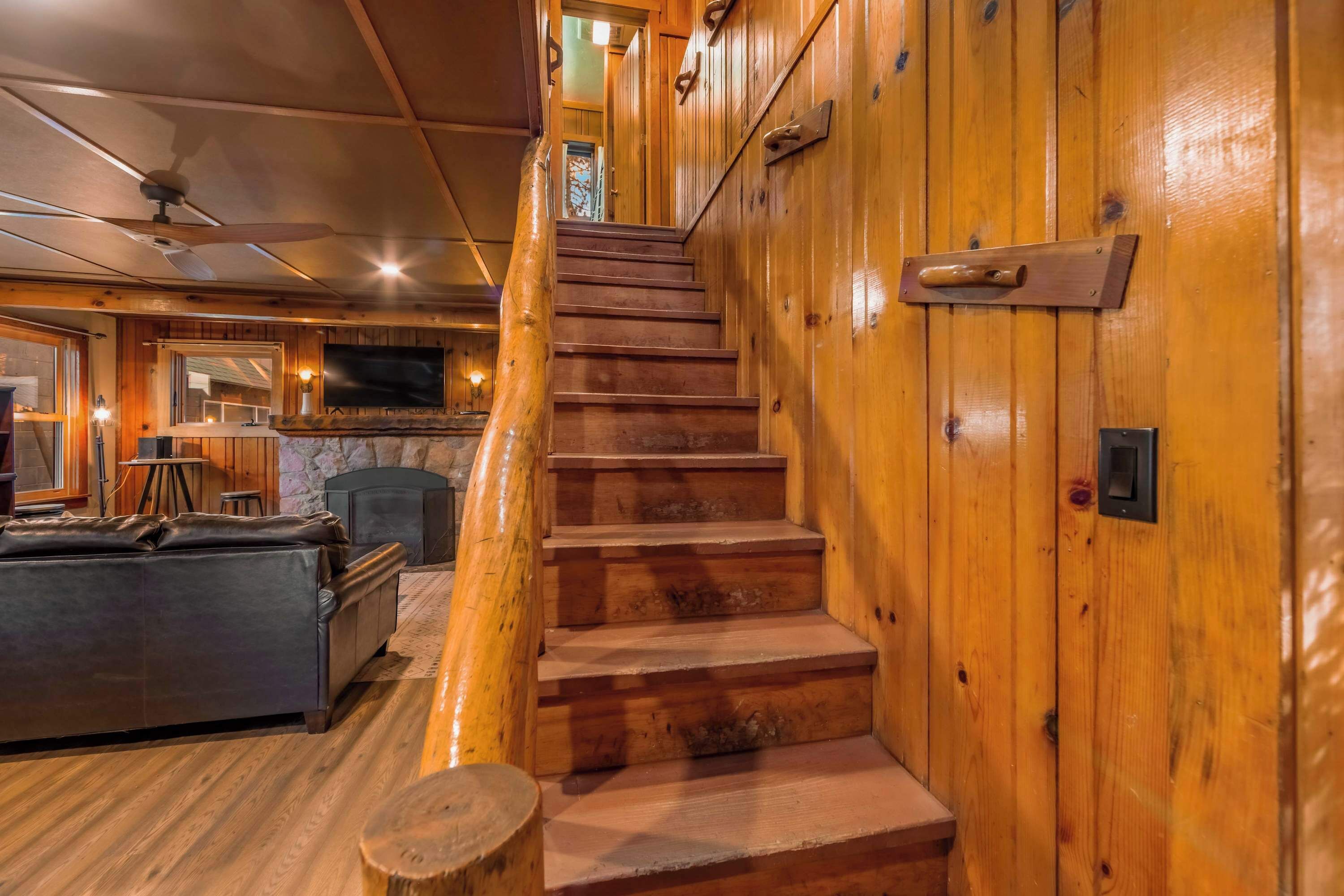 Un intérieur en bois avec un escalier menant à un deuxième étage, une cheminée, un canapé en cuir et un téléviseur.