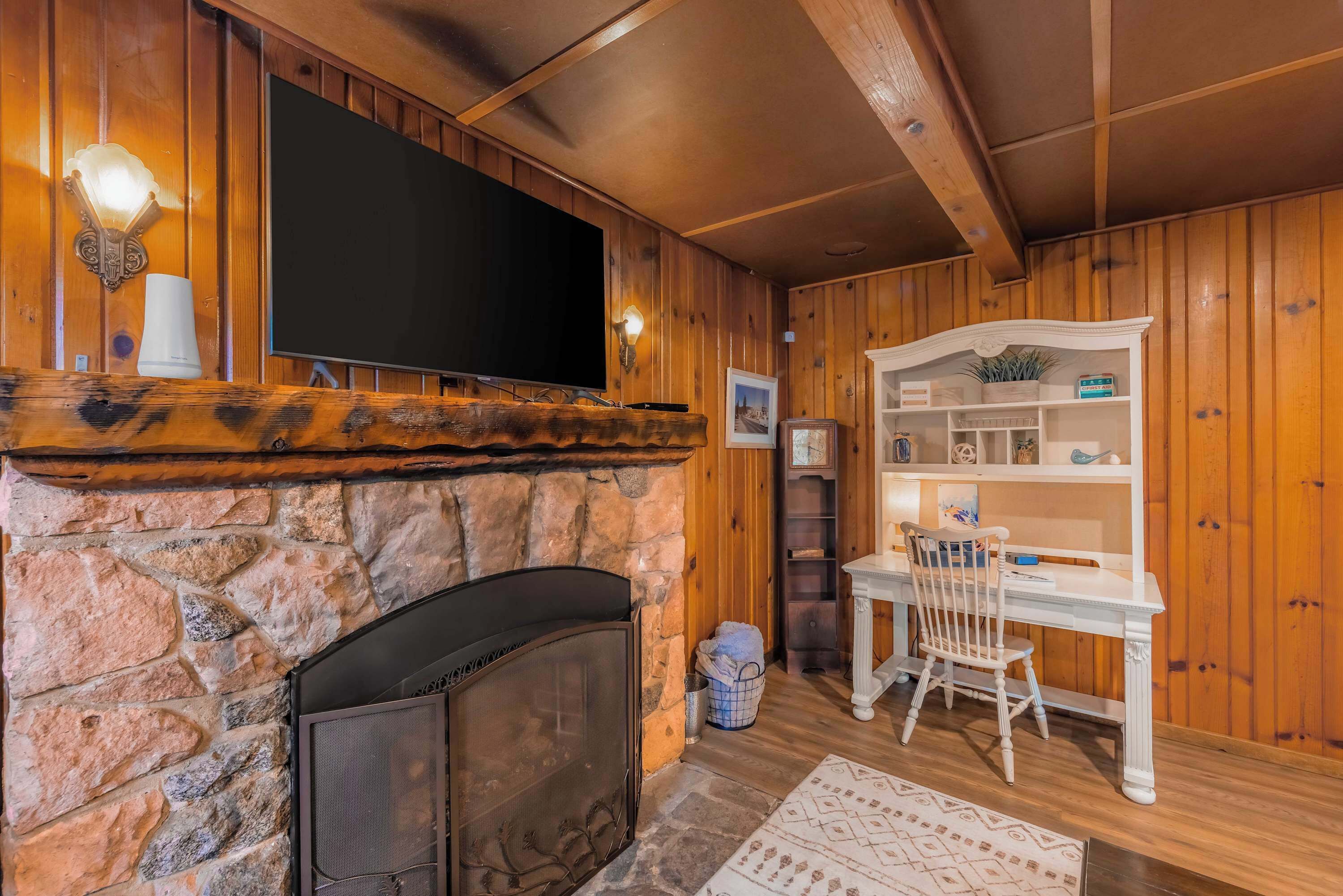 A cozy room with a stone fireplace, a television mounted on the wall, and a wooden ceiling.