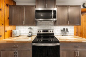 A kitchen with wooden cabinets, a stainless steel microwave, a black stove, and a coffee maker. - Bearfoot Cabin - Central Tahoe Cabin (South Lake Tahoe)