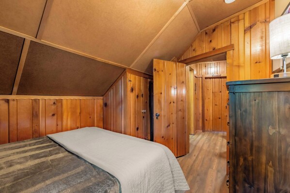A bedroom with a bed, wooden walls, a door, and a dresser. - Bearfoot Cabin - Central Tahoe Cabin (South Lake Tahoe)