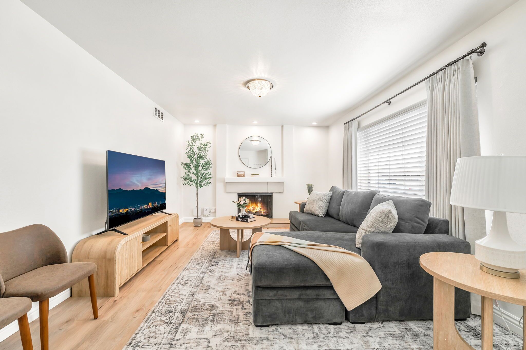 Una sala moderna con televisión de pantalla plana, sofá gris, mesa de centro de madera y chimenea.