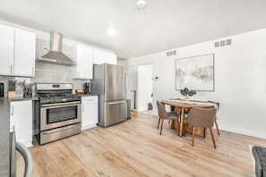 A modern kitchen with stainless steel appliances, a dining area with a wooden table and chairs, and a minimalist wall art piece.