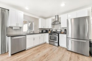 A modern kitchen with white cabinets, stainless steel appliances, and a wooden floor. - Modern 3 bd Oasis, Pool, Spa, Fire Pit, Vegas Strip, Allegiant Stadium (Las Vegas)