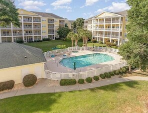 Ein Hotel mit Schwimmbad, umgeben von einer weißen Einfriedung, mehreren Balkonen und einem gepflegten Rasen.