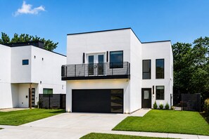 Een modern herenhuis met twee verdiepingen, een plat dak, een balkon met zwarte leuning en een garage.
