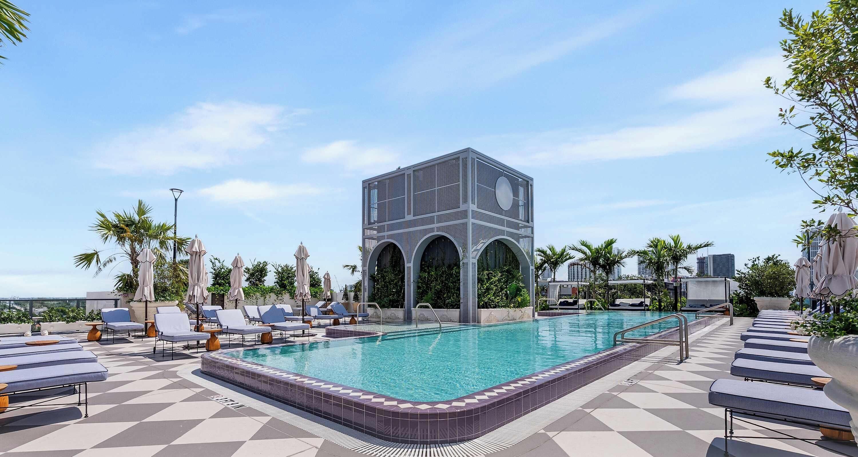 Une piscine sur le toit, agrémentée de chaises longues, un bâtiment moderne aux arches élégantes et un ciel dégagé.