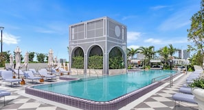 A pool area with lounge chairs, a central water feature, and a distinctive arched structure. - Rooftop Bar & Pool in NoMad Residences Wynwood (Miami)