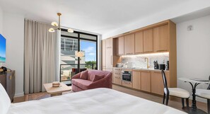 Ein modernes Hotelzimmer mit Bett, einer Sitzecke, einer Küchenzeile und einem großen Fenster mit Blick auf die Stadt.