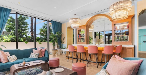 A modern living room with a sofa, coffee table, and ottomans. There is a bar area with stools and a mirror. - Studio w/ Rooftop Pool in NoMad Residences Wynwood (Miami)