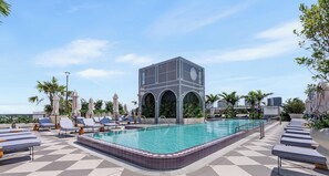 Zona d'una piscina al terrat amb gandules, un edifici modern amb arcs i un cel serè.