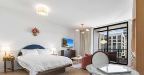Una habitación de hotel con una cama, lámparas de noche, un escritorio, una silla, vistas a edificios y un cuadro en la pared.