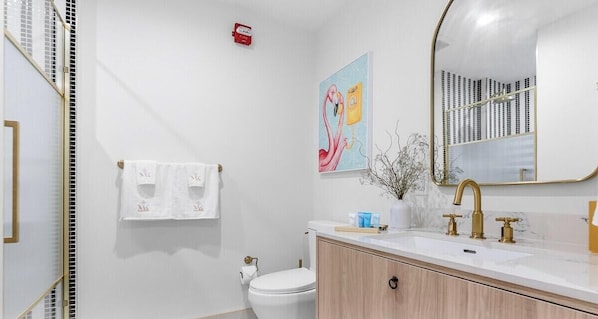 A bathroom with a white toilet, a sink with gold fixtures, and a mirror with a gold frame. - 2BR w/ Pool Access in NoMad Residences Wynwood (Miami)