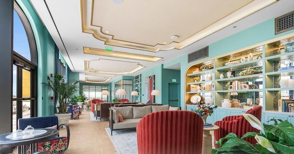 En hotellobby med siddeområde, en reol og et stort vindue.