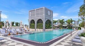 A swimming pool with lounge chairs and umbrellas, surrounded by greenery and a modern building structure. - 2BR w/ Pool Access in NoMad Residences Wynwood (Miami)