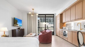 A hotel room with a bed, a desk, a chair, a kitchen area, and a large window with a view. - 2BR w/ Pool Access in NoMad Residences Wynwood (Miami)