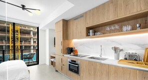 A modern kitchen with wooden cabinets, a built-in oven, and a marble countertop. - The Crosby | Miami World Center (Miami)