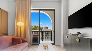 A modern hotel room with a sofa, a flat-screen TV, a sliding glass door to a balcony, and a view of buildings. - Rooftop Restaurant in NoMad Residences Wynwood (Miami)