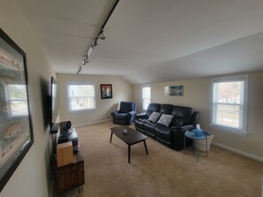 Ein Wohnzimmer mit einer schwarzen Ledersofa, einem Couchtisch, einem Fernseher und einem gerahmten Bild an der Wand.