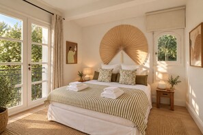 A bedroom with a large bed, two bedside tables with lamps, a window with a view of greenery, and a wall-mounted fan. - Villa Vany - Provence & View (Éguilles)