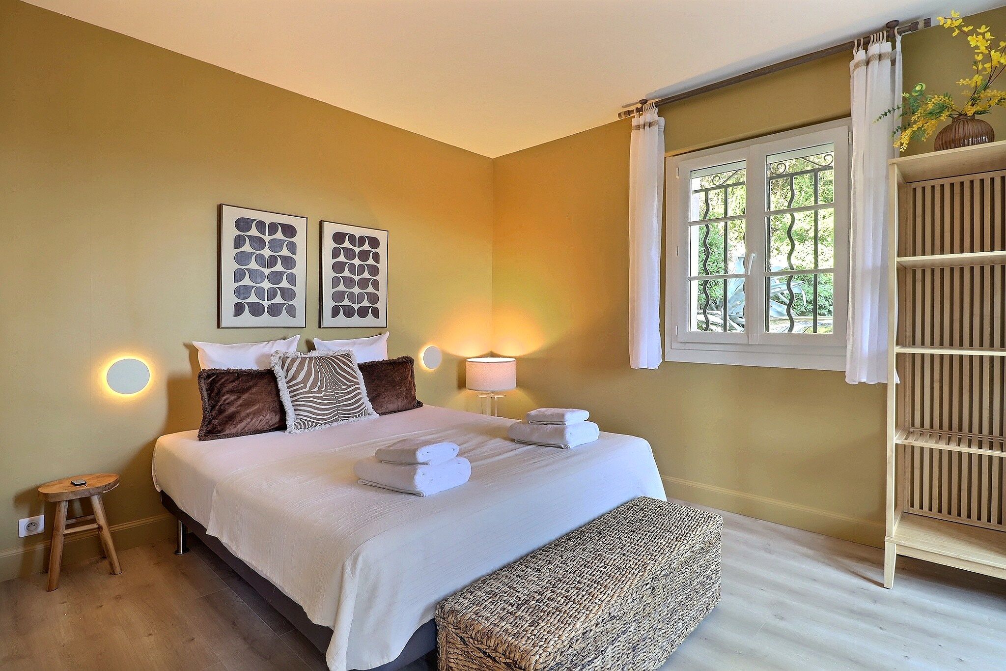 A bedroom with a bed, bedside tables, a window with curtains, and wall art.