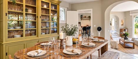 Un comedor con una mesa de madera dispuesta para cuatro personas, rodeado por un aparador verde con puertas de cristal.