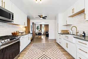 A modern kitchen with white cabinetry, a gas stove, and a ceiling fan. - South Bay Hideaway - 3BR/2BA Near LAX, Beaches & SoFi - Monthly Stays (Lawndale)